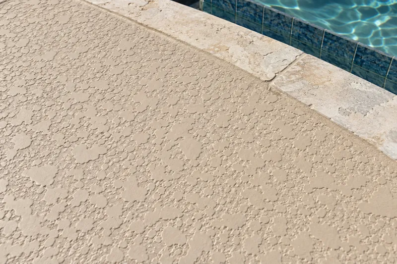 Light tan splashed cool deck texture beside pool coping