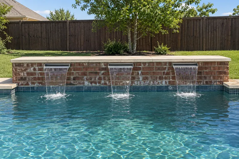 Three sheer-descent waterfalls pouring from a raised brick wall into a pool